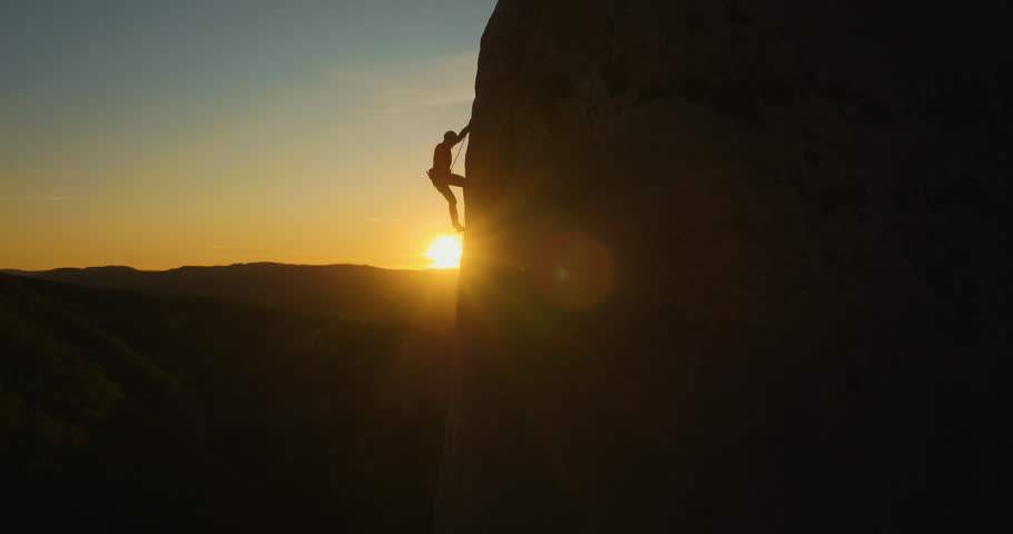 Aerial of a man silhouette climbing up the wall at amazing sunset.