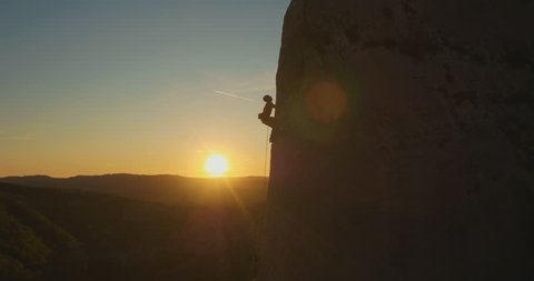 Aerial fly-by a man rock climbing outdoors at amazing sunset.