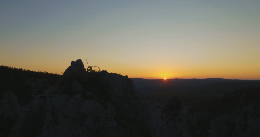 Aerial circling around solo climber celebrating on the top of the mountain at sunset.