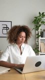 Vertical video of multiracial woman working using laptop and writing down notes on planner. Working from home.