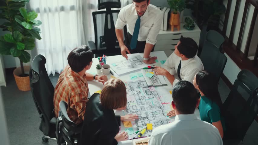 Group of diverse team planning strategy while sitting at table with project plan. Top aerial view of smart business people working together to brainstorm and design house construction. Alimentation. Royalty-Free Stock Footage #3492700891