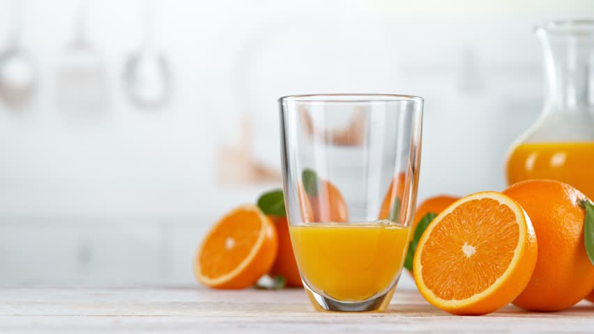 Super slow motion of pouring orange juice into glass. Placed on white table with kitchen interior. Filmed on high speed cinema camera, 1000 fps.