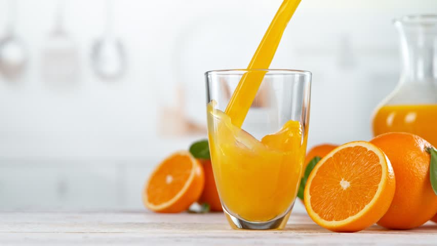Super slow motion of pouring orange juice into glass. Placed on white table with kitchen interior. Filmed on high speed cinema camera, 1000 fps.