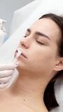 Vertical video. Cosmetology clinic, the doctor applies anesthesia to the patient's lips, anesthetic before injecting hyaluronic acid. Before the injection procedure, an anesthetic ointment is applied.