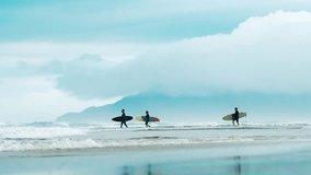 Surfers with surf boards walk into the ocean with foggy mountains on the background - Powered by Shutterstock - Get 15% off with code: PIKWIZARD15