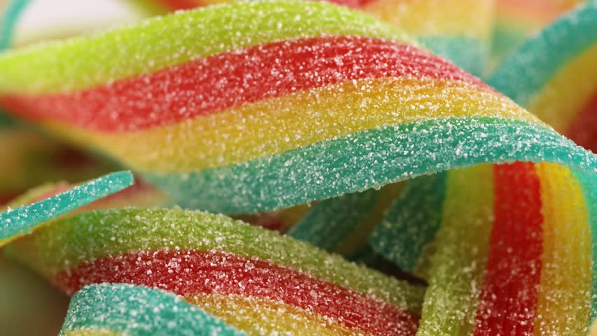 Colorful jelly candies strips in sugar sprinkles. Sour flavored rainbow candy background.