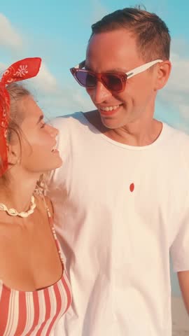 Young laughing Caucasian couple of man and woman walk along beach telling funny stories from life and pointing with finger ahead planning future vacation located on picturesque island in ocean.