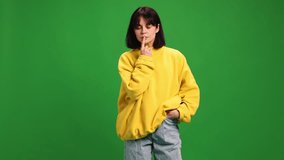 Young brunette woman with short hair posing in yellow sweatshirt and looking at camera against vibrant green studio background. Concept of human emotions, fashion, beauty, style.