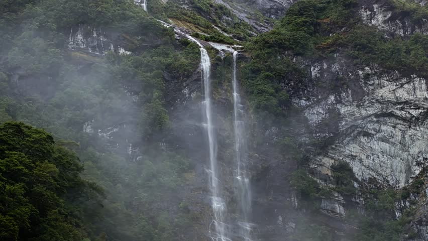 Aerial telephoto of mist and clouds obscuring waterfall cascading down escarpment of Milford Sound