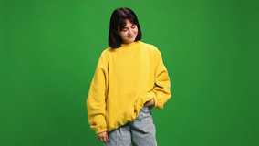 Young smiling woman with short hair posing in yellow sweatshirt and looking at camera against vibrant green studio background. Concept of human emotions, fashion, beauty, style.