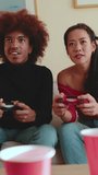 Vertical video, Young couple with gamepads playing video game at home sitting on the sofa in cozy living room