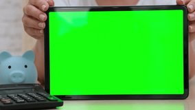 Woman showing big green screen tablet near light blue piggy bank and calculator. Online banking and accounting concept - Powered by Shutterstock - Get 15% off with code: PIKWIZARD15