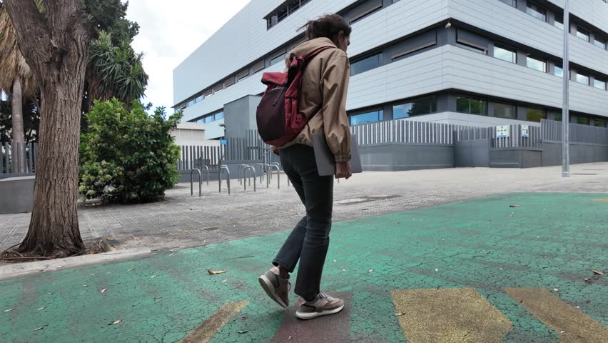 A Latin-American woman strolls through the university campus with her laptop and backpack on a sunny day, heading to classes. University student life, education, and future