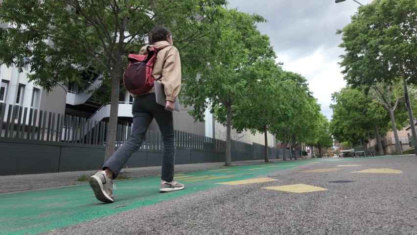 A Latin-American woman strolls through the university campus with her laptop and backpack on a sunny day, heading to classes. University student life, education, and future