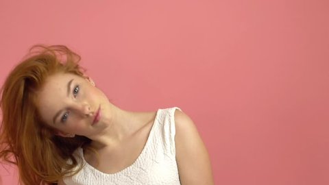 Beautiful teenage girl with red blowing hair and blue eyes on pink background