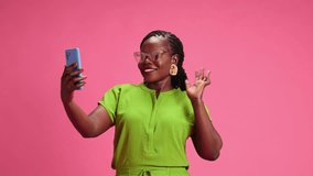 Portrait of young African-American woman talking on phone in red neon light against pastel pink studio background. Concept of human emotions, fashion and beauty, trends, communication.