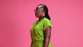 Cheerful African-American woman dressed vibrant attire looking at camera with smile against pastel pink studio background. Concept of human emotions, fashion and beauty, trends, sales season.