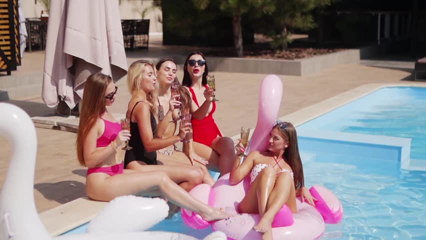 Women drink champagne sitting at swimming pool in swimsuits, bikini, clink glasses. Lady chills out on inflatable flamingo in luxury club toasting cocktails. Models in sunglasses relax having fun. Royalty-Free Stock Footage #3493064661
