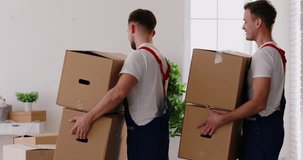 Young cheerful professional workers of moving service in overalls carrying and delivering cardboard boxes in new apartment. Move, moving day and relocation concept. 4k video. Slow motion video.