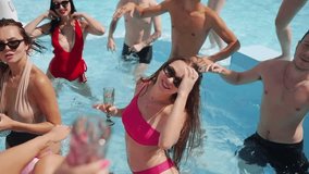 Female and male models chilling in swimming pool, splashing water, flirting and posing for photoshoot. Group of friends in swimsuits and sunglasses have fun and relax on summer holidays. - Powered by Shutterstock - Get 15% off with code: PIKWIZARD15