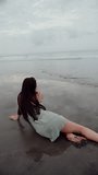 brunette girl lying on the sand and running from the wave, vertical video