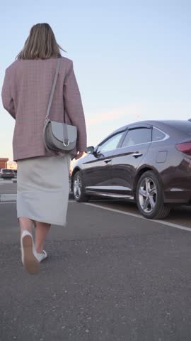 A business woman with a handbag in a fashionable business suit gets into a car in the parking lot