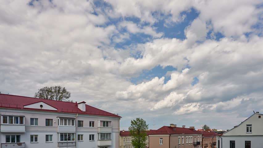 A timelapse of clouds over the city. Clouds float over the roofs of houses in a cozy city on a warm sunny day. Summer in the city.
