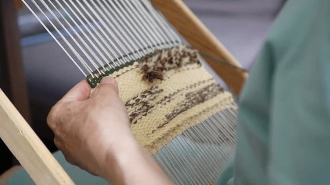 Woman creating small-format tapestry piece using hand loom and weft beater, selective focus. Pushing weft threads down with wooden tapestry beater Stockvideó