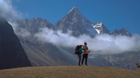 Hikers with backpacks travel in the Himalayan mountains. The map helps you to choose the right path. 4K