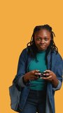 Vertical video Euphoric african american woman playing intense gaming console game, celebrating win, studio background. Ecstatic young girl using controller, excited after being victorious in