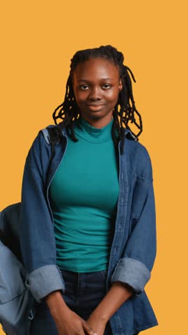 Vertical video Upbeat african american teenager goofing around, feeling joyous, isolated over studio background. Portrait of happy young girl acting silly, showing positive demeanor, camera B Royalty-Free Stock Footage #3493187891