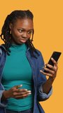 Vertical video Upset african american woman arguing with friends during teleconference meeting on smartphone, studio background. Annoyed girl fighting on mobile phone videocall with mates, camera A