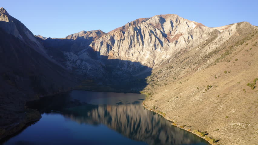 Aerial Convict Lake Between Rock Formations, Drone Flying Backwards Over Landscape On Sunny Day - Mammoth Lakes, California