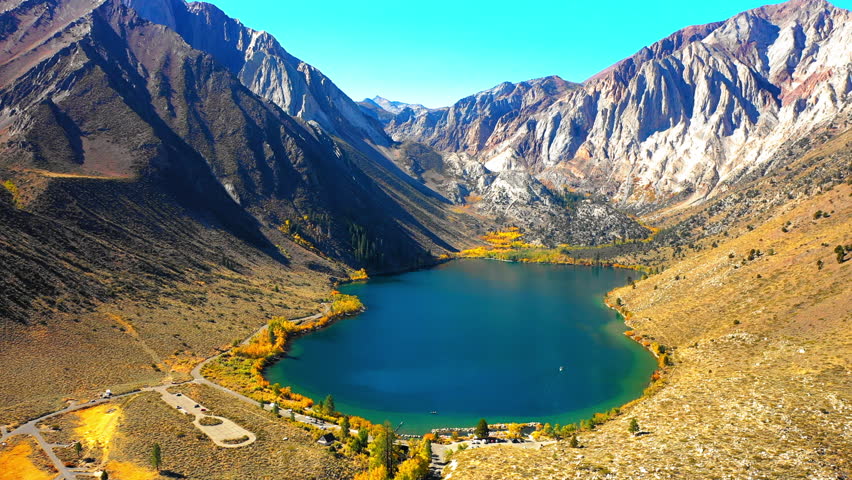 Aerial Shot Of Tranquil Convict Lake Amidst Rock Formations Against Clear Sky, Drone Flying Backwards Over Landscape On Sunny Day - Mammoth Lakes, California