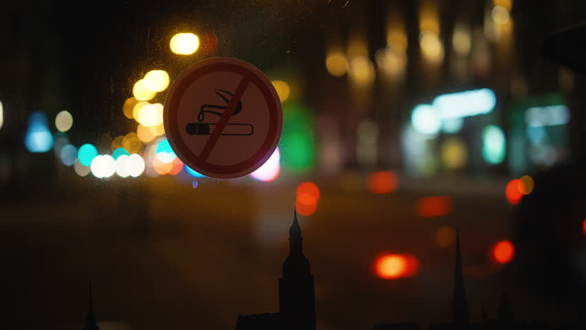 City lights: No smoking sign on window with stunning blurry urban background at nighttime