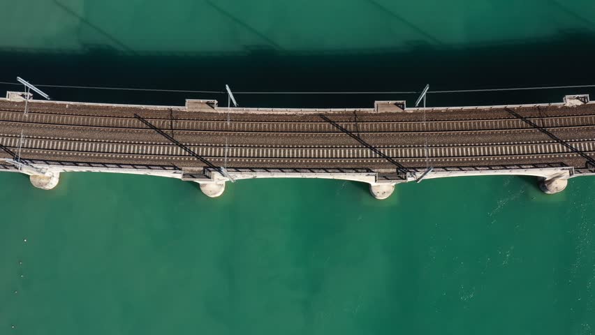 Train on the bridge over the river aerial view. Red high-speed train top view, slow motion on an arched bridge over a mountain river in Italy. Red train in Europe. Arched bridge over the water.