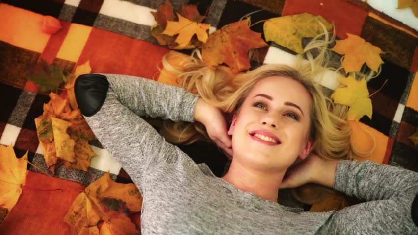 a blonde girl lies on a plaid in a cage and on top fall autumn leaves