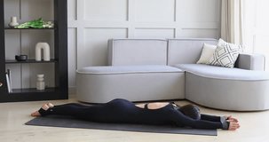 A woman performs the Shalabhasana exercise with her arms extended forward, a variation of the locust pose, practicing yoga lying on a mat in black sportswear, full-length view