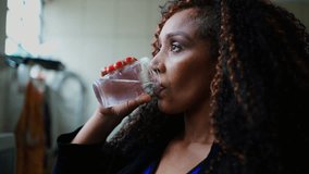 One thoughtful black middle-aged woman drinking water while gazing in the distance with pensive emotion. Contemplative latina person of African descent hydrating herself - Powered by Shutterstock - Get 15% off with code: PIKWIZARD15