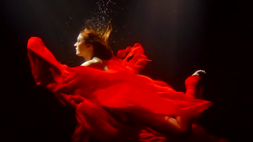 mystical redhead undine is floating underwater with red fabric around in dark deepness of river