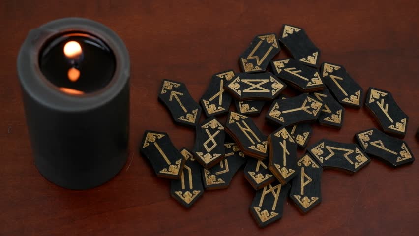 Burning black witch candle and black runes on wooden table.	