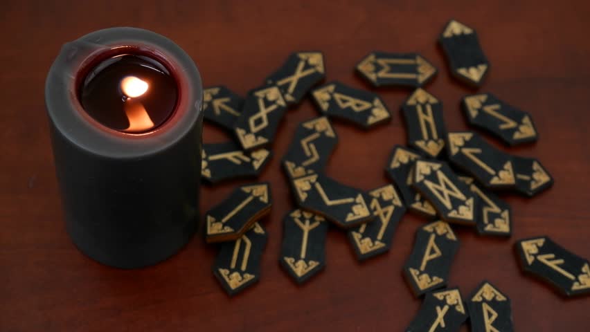 Burning black candle and human hand shows several runes close-up.