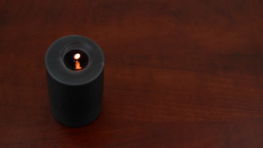 Burning black candle and black runes on wooden table. Human hand taking several runes, fortune telling concept.