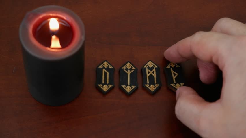 Burning black candle and runes on wooden table. Human hand choosing different runes, fortune telling con,cept.