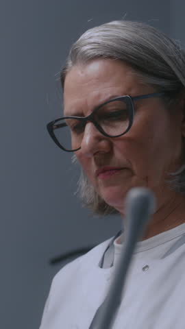 Mature female doctor looks at monitor of ultrasound machine while doing sonography diagnostics. Medical specialist performs check up or examination in modern clinic using advanced equipment. Vertical Royalty-Free Stock Footage #3493546729