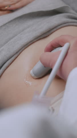 Vertical shot of professional doctor doing stomach sonography check up procedure using advanced medical equipment. Patient undergoes ultrasound diagnostics of abdominal organs in modern clinic or Royalty-Free Stock Footage #3493619955