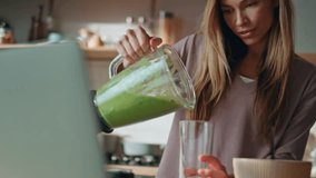 Woman recording culinary blog at laptop camera in home kitchen close up. Smiling attractive girl pouring green vegetables smoothie in glass looking computer webcam. Happy housewife cooking breakfast. - Powered by Shutterstock - Get 15% off with code: PIKWIZARD15