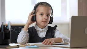 Caucasian child girl wear headphones, using laptop sitting writing listening tutor online virtual lesson studying at home