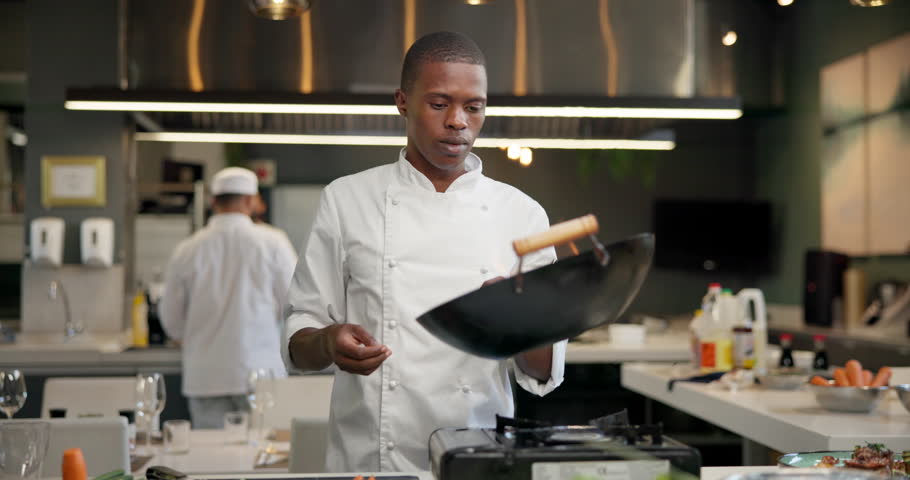 Chef, black man and pan on fire in kitchen for cooking with speed, professional and enhance flavor or taste. Person, serious and roast with flame for frying, gastronomy and culinary techniques.