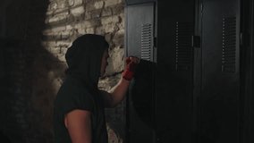 Male boxer in green hoodie prepares for training, hanging up his boxing gloves in dimly lit locker room with rustic brick wall - Powered by Shutterstock - Get 15% off with code: PIKWIZARD15